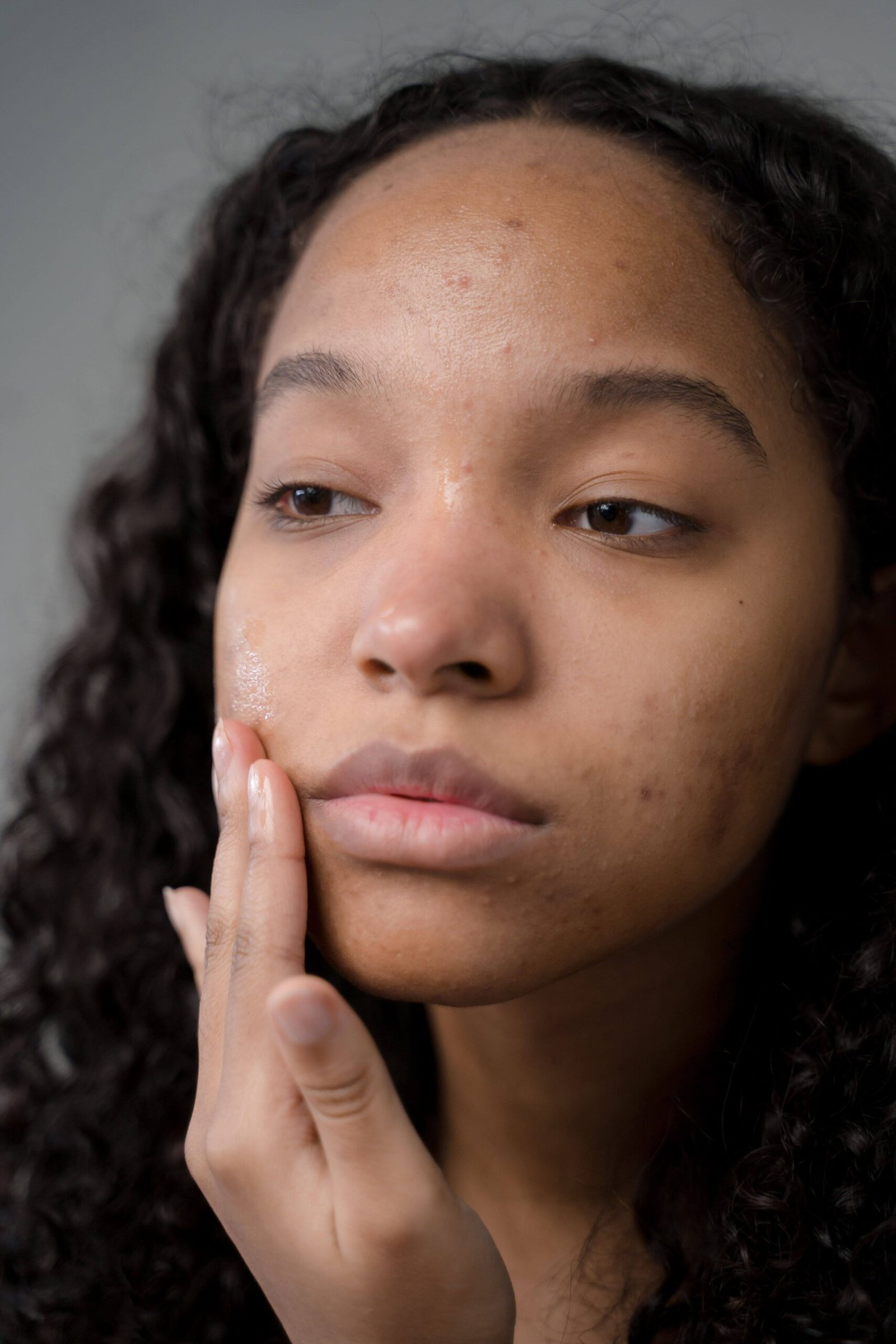 Skin type vs skin condition: caramel-skinned woman touching her face while looking in the mirror